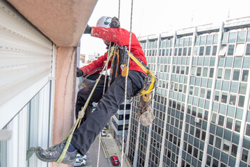 trabajador en altura o trabajador vertical arreglando una fachada frente a un edificio de oficinas