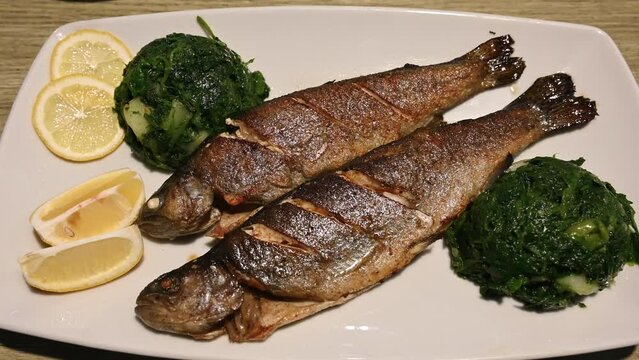 Grilled trout served on plate in restaurant. Tasty fish served with potato and spinach. Delicious roasted fish prepared for dinner. 