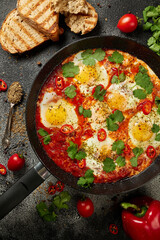Tasty Shakshuka eggs in a pan with toast on a dark concrete background. Eggs poached  in a spicy tomato pepper sauce. Traditional Jewish scrambled eggs. Flat lay, Top view.