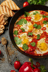Tasty Shakshuka eggs in a pan with toast on a dark concrete background. Eggs poached  in a spicy tomato pepper sauce. Traditional Jewish scrambled eggs. Flat lay, Top view.