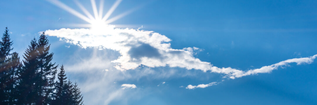 The sun shines through fluffy clouds against a blue sky