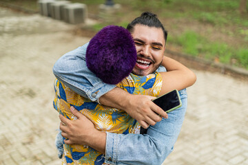 Top view image of two smiling gay friends greeting each other with a big hug in the open air. 