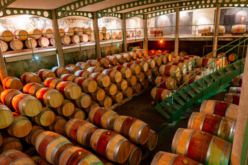 Obraz premium French oak wooden barrels for aging red wine in underground cellar, Saint-Emilion wine making region picking, cru class Merlot or Cabernet Sauvignon red wine grapes, France, Bordeaux