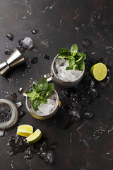 Two silver mugs of moscow mule or mint julep cocktail with crushed ice, mint and lime on dark...