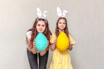 Happy Easter. Two girls wearing Easter bunny ears hold Easter eggs in their hands. Copy space.