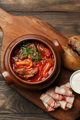 Warming beetroot soup with beef and mushrooms served on wooden board with rye bun, sour cream and bacon. Traditional Russian and Ukrainian soup borsch. Overthead view