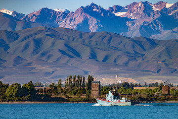 A boat on the water of the famous Issyk-Kul lake surrounded by the Ala-Too mountains. Kyrgyzstan, July 2023