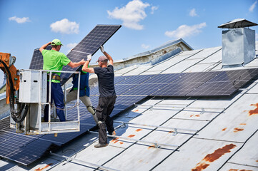 Workers lifting up photovoltaic solar panel on metal rooftop of house with assistance of crane lift. Men installers installing photovoltaic solar modules outdoors. Renewable energy generation concept. © anatoliy_gleb