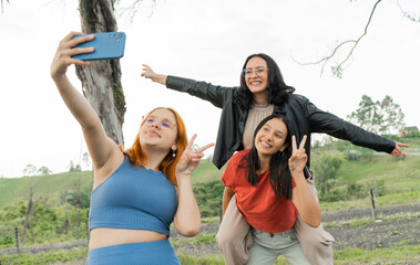 grupo pequeño de mujeres jóvenes sonriendo y al aire libre jugando mientras se hacen una selfie...