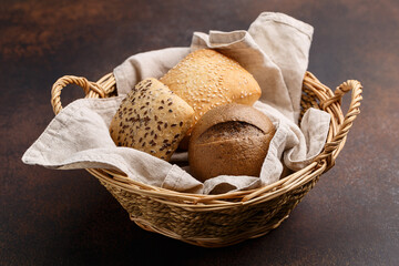 Different kinds of freshly baked buns. White, multigrain and rye buns in wicker basket on dark...