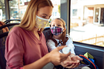 Mother using hand sanitizer on daughters hands on the bus