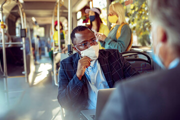Businessman with face mask working on laptop on public transport