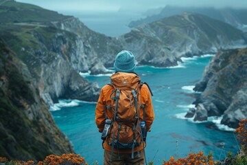 An individual hiker in an orange jacket stands taking in the view over a dramatic coastline with...