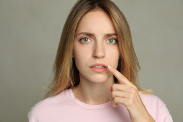 Woman with herpes applying cream onto lip against  light grey background