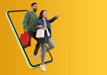Online shopping. Happy couple with paper bags walking out from smartphone on orange background,...
