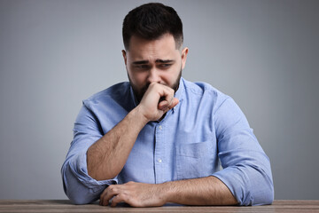 Portrait of sad man at wooden table on light grey background
