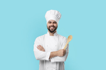 Happy young chef in uniform holding wooden spoon on light blue background