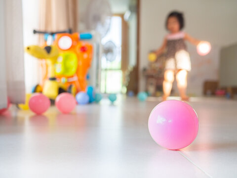Close-up pink plastic ball placed on white floor in house There is a blurred image in the background of a child playing with children's toys. For the concept of child development.