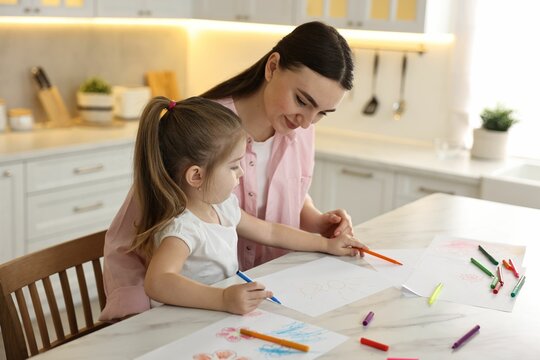 Mother and her little daughter drawing with colorful markers at table in kitchen