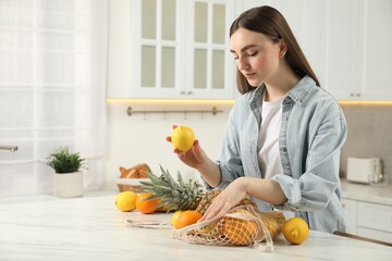Obraz premium Woman with lemon and string bag of fresh fruits at light marble table in kitchen