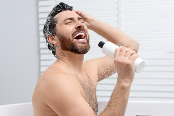 Happy man with bottle of shampoo singing in shower