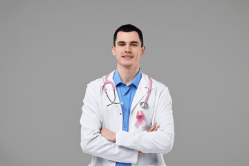 Fototapeta premium Portrait of smiling mammologist with pink ribbon and stethoscope on grey background. Breast cancer awareness