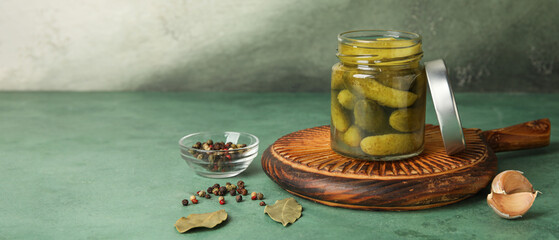 Jar of tasty pickled cucumbers and spices on green background with space for text
