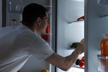 Fototapeta na wymiar Man near refrigerator in kitchen at night