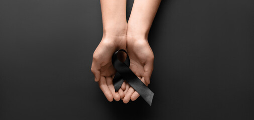 Woman holding black funeral ribbon on dark background