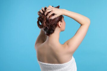 Young woman washing her hair with shampoo on light blue background, back view