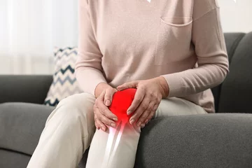 Rolgordijnen Arthritis symptoms. Woman suffering from pain in her knee on sofa indoors, closeup © New Africa