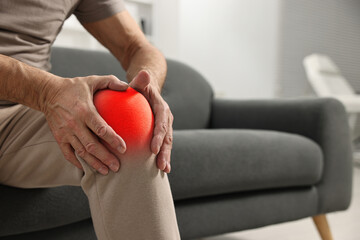 Arthritis symptoms. Man suffering from pain in his knee on sofa indoors, closeup. Space for text