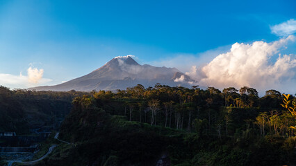 The beauty of Mount Merapi at dusk before dark with a cliff of cold lava flows right in front of it. Mount Merapi looks detailed on a clear day with blue sky and clouds beside it