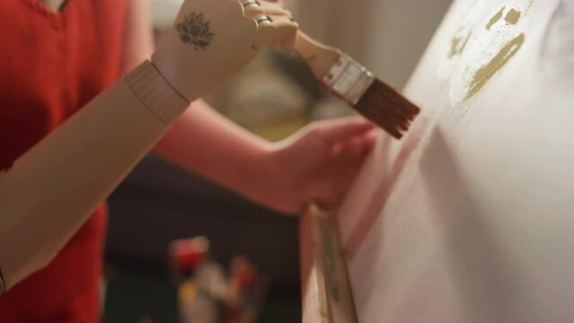 Side tilt closeup of Caucasian girl in glasses creating artwork with wide brush on canvas using bionic hand at home