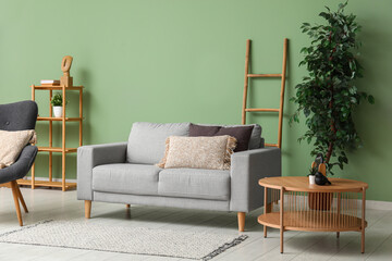 Cozy grey sofa, plants and coffee table near green wall