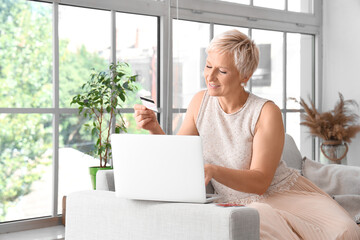Mature woman with credit card and laptop shopping online at home