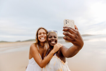 two friends having a good time on the beach taking selfie pictures with their smart phone during a...