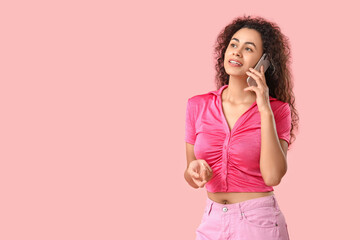 Young African-American woman talking by phone on pink background