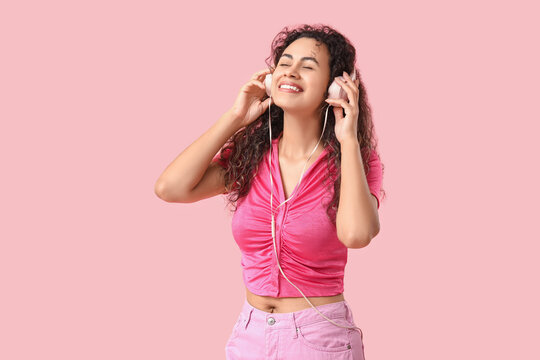 Fototapeta Young African-American woman with headphones listening to music on pink background