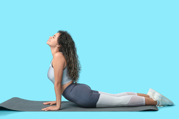 Fototapeta premium Young African-American woman practicing pilates on blue background