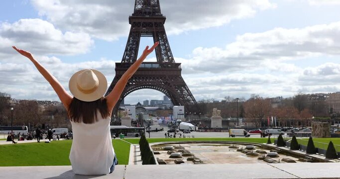 A happy tourist woman enjoys the beautiful view of the Eiffel Tower in Paris, France, during a sunny spring day