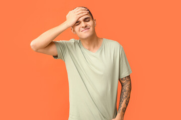 Handsome ashamed young man covering face with hand on orange background