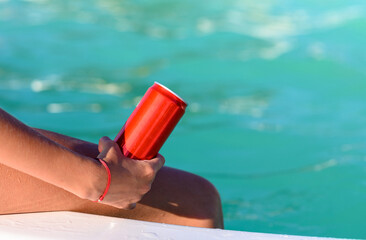 A red can with a drink in the hand of a girl by the pool. Close-up