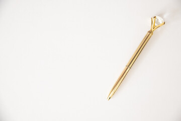 Caneta dourada sob fundo branco com  diamante na ponta da caneta