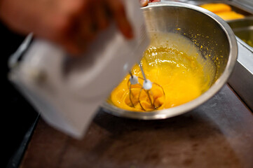 A person using an electric mixer to blend a yellow batter in a stainless steel bowl