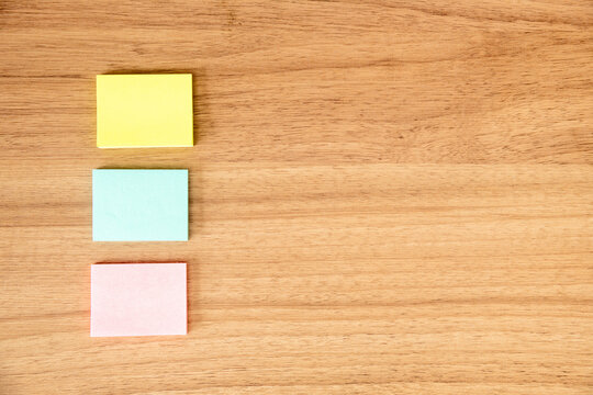 Post it, papel de recado sob fundo de madeira bege. Amarelo rosa azul. tr&ecirc;s papeis, espa&ccedil;o para deixar recado, escrever noticia, redes sociais