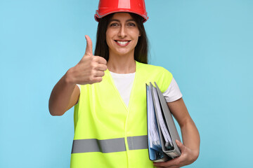 Architect in hard hat with folders showing thumbs up on light blue background