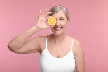 Beautiful woman with half of orange rich in vitamin C on pink background