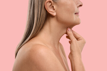 Obraz na płótnie Canvas Mature woman touching her neck on pink background, closeup