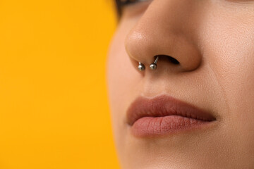 Stylish young woman with nose piercing on yellow background, closeup